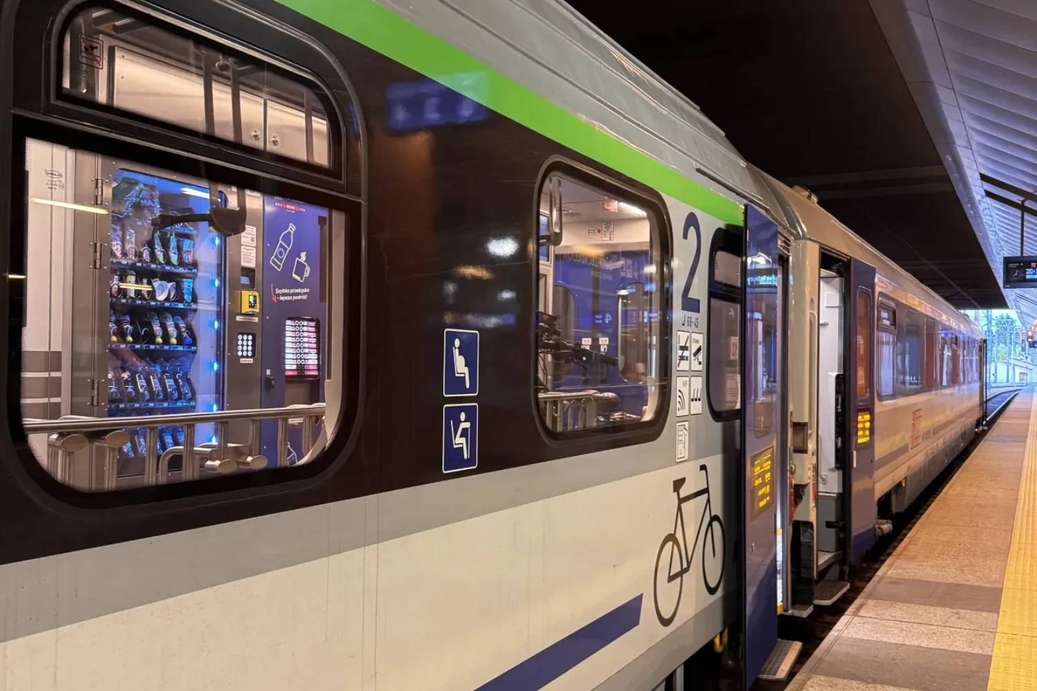 Podświetlony automat Quatro Vend w pociągu Intercity widoczny z peronu przez szybę wagonu.