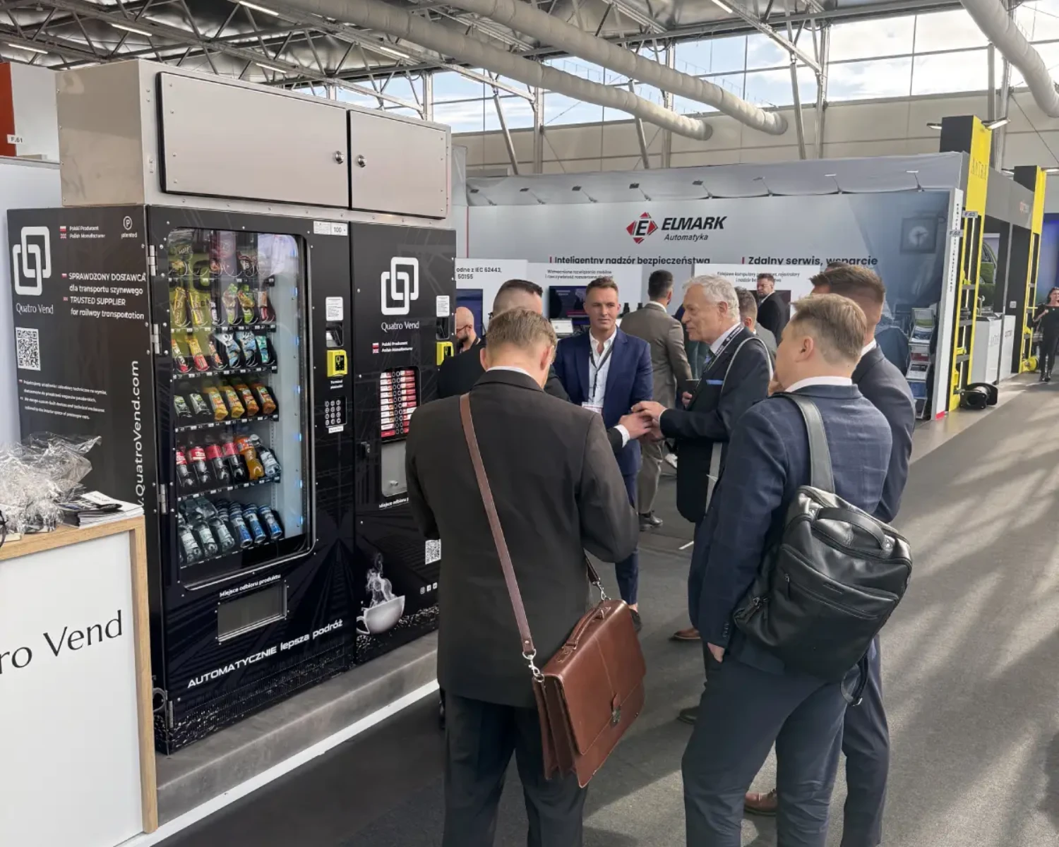 Grupa biznesmenów ogląda automaty vendingowe Trako 2025 od Quatro Vend.